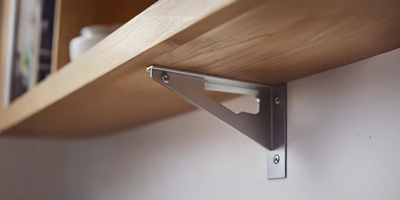 Repisa de madera instalada en la pared con un soporte metálico triangular y tornillos visibles.