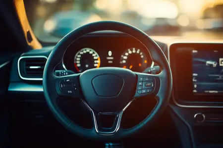 Manubrio de un auto de color gris. Se aprecia el tablero del vehículo con luces blancas y rojas.